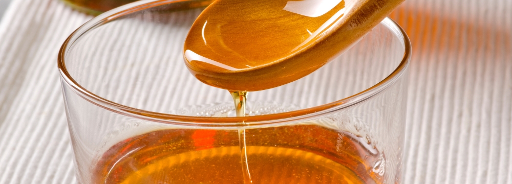 Spoon with dripping agave syrup into clear bowl