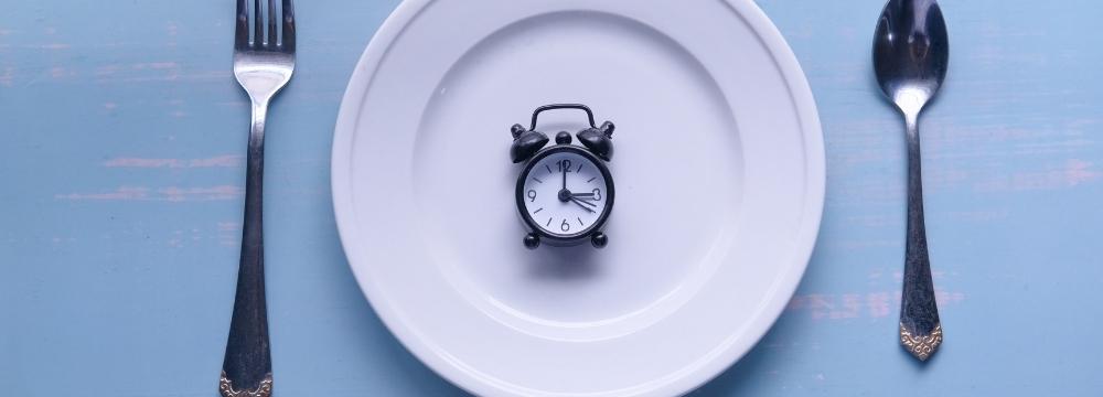 place setting with spoon, fork and plate, with a small clock sitting on plate