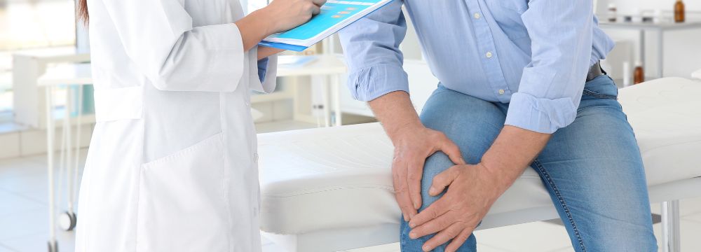 man on doctor table holding knee while doctor takes notes on clipboard