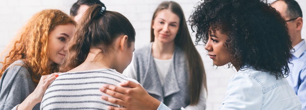 Woman in therapy circle being comforted by peers