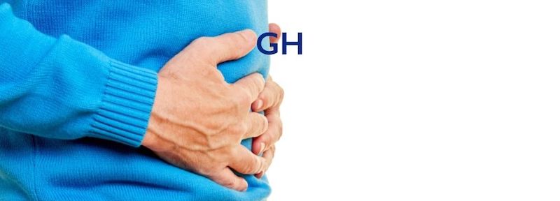 Man holds abdomen in discomfort after a fatty meal due to his dumping syndrome after weight loss surgery