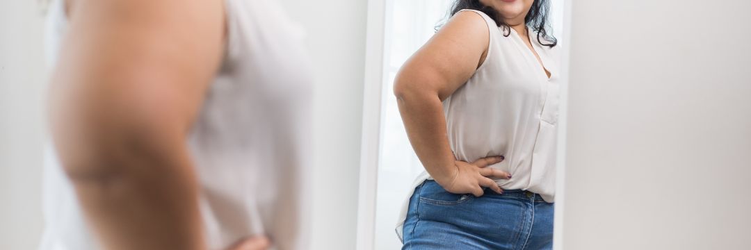 Woman looking at herself in mirror with hands on hips and smiling 