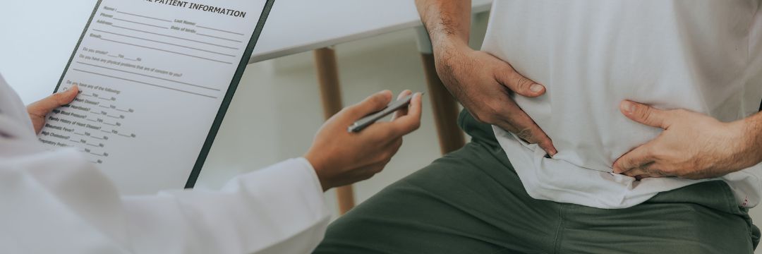 Man on doctor's table pointing to hernia pain while doctor makes notes