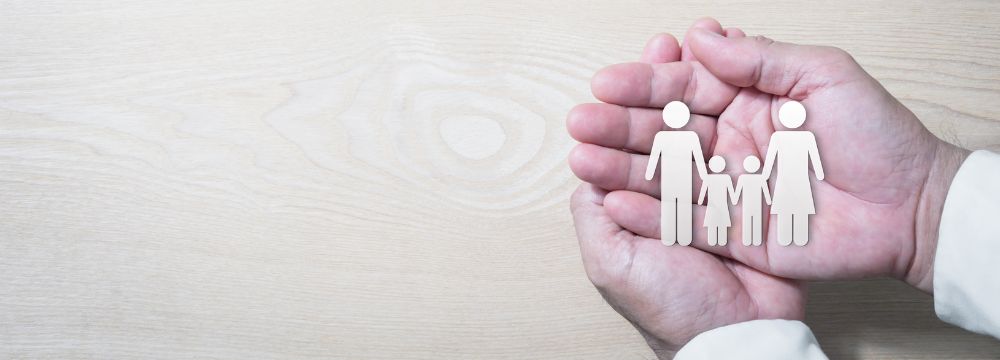 person holding paper cutout of family in palms of crossed hands