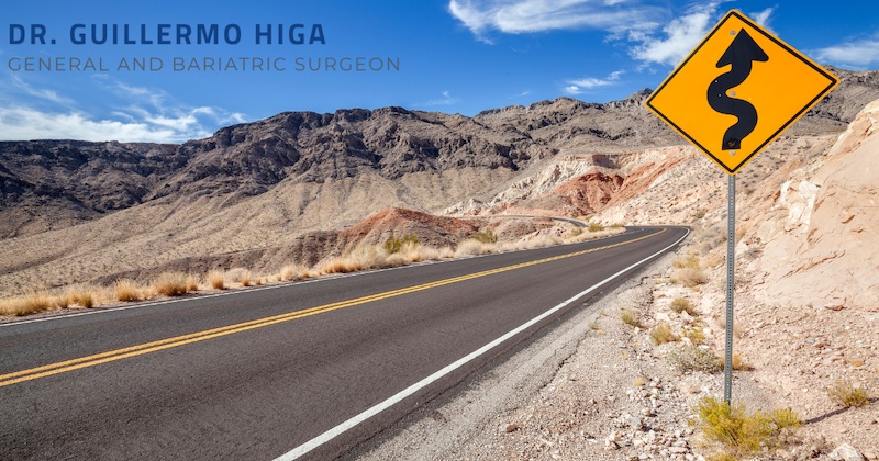 Asphalt Rode with a Yellow winding Road Sign And Mountains in the background 