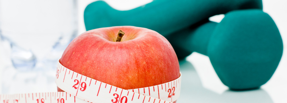 Measuring tape wrapped around an apple in-front of teal dumbbells