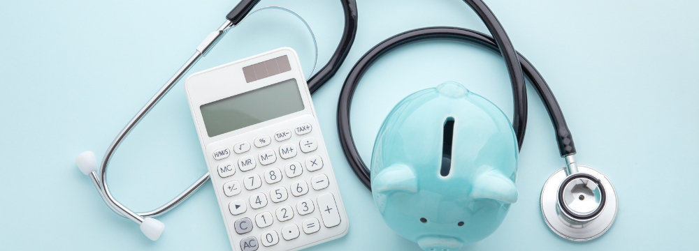 piggy bank, calculator and stethoscope lie infront of a light blue backdrop